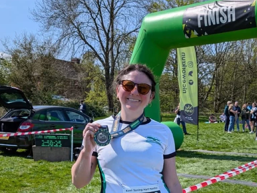 Maidstone Harriers runner, Kate Phillips-Barrett, smiling with finisher medal under the Kent Spring Half Marathon finish arch.