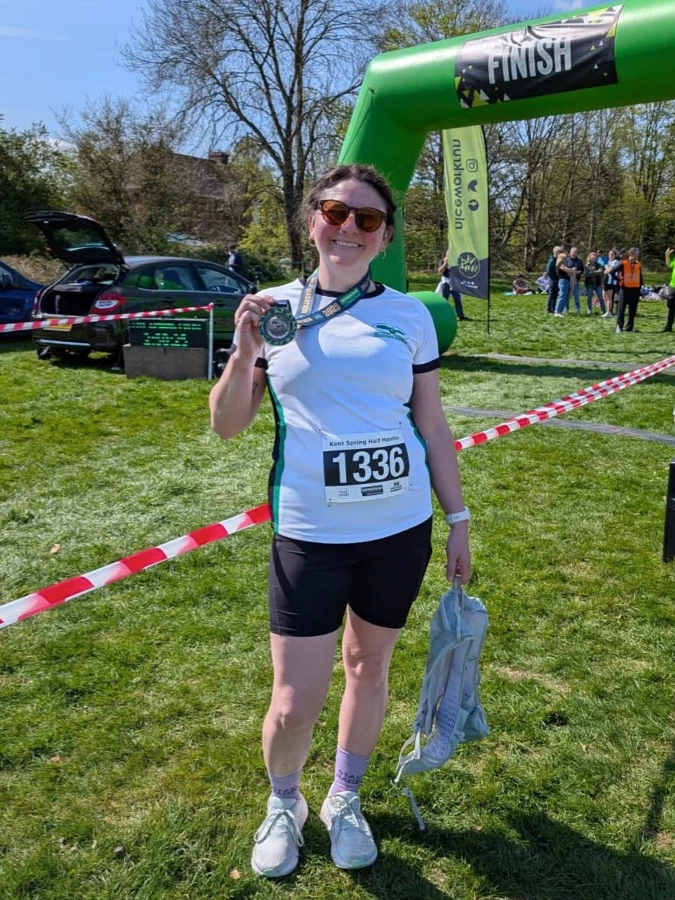 Maidstone Harriers runner, Kate Phillips-Barrett, holding finisher medal at the Kent Spring Half Marathon finish, race bib 1336.