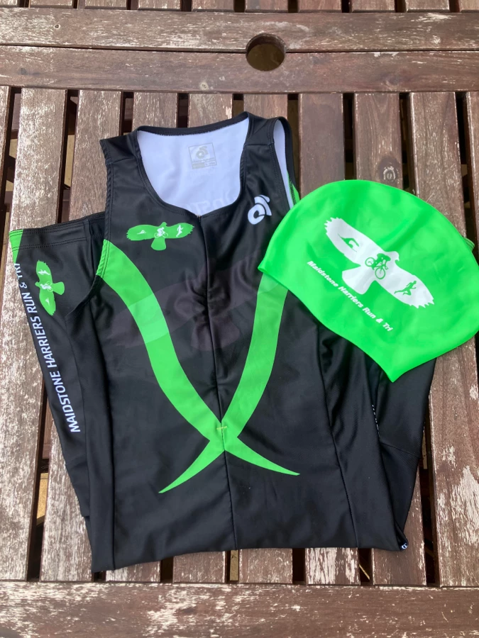 Kate's Maidstone Harriers tri vest and green swim cap on a wooden table.