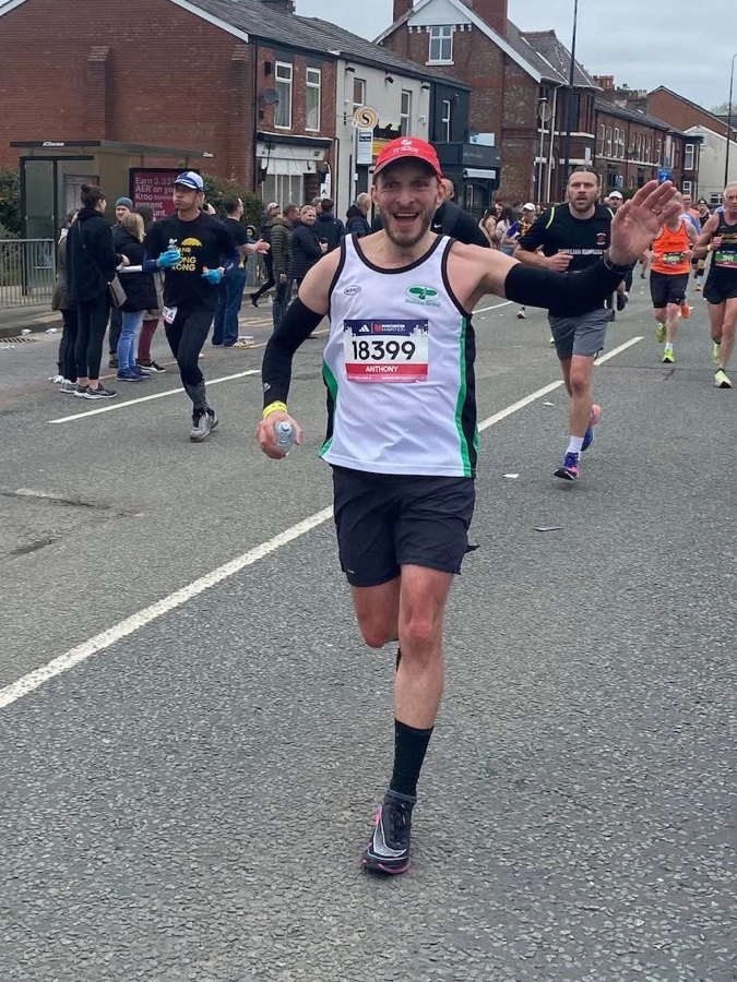 Anthony Warren running on a town centre road in a Maidstone Harriers vest, smiling and waving to the crowd