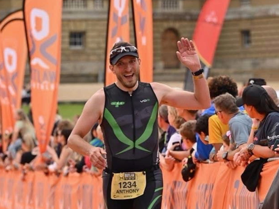 Anthony Warren celebrating on the orange finish carpet at an Outlaw Triathlon event, wearing Maidstone Harriers tri kit.