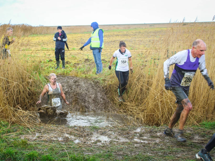 Runners crossing a muddy dyke at KFL Minnis Bay.