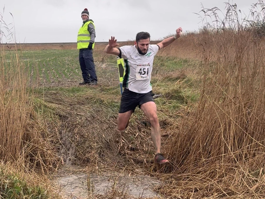 KFL Minnis Bay 2024 - Kent Fitness League runners in action crossing a muddy ditch. Ryan Worsley of Maidstone Harriers