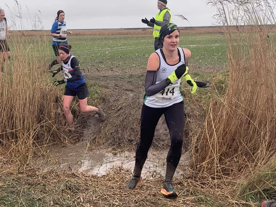 KFL Minnis Bay 2024 - Kent Fitness League runners in action crossing a muddy ditch. Trudi Hood of Maidstone Harriers