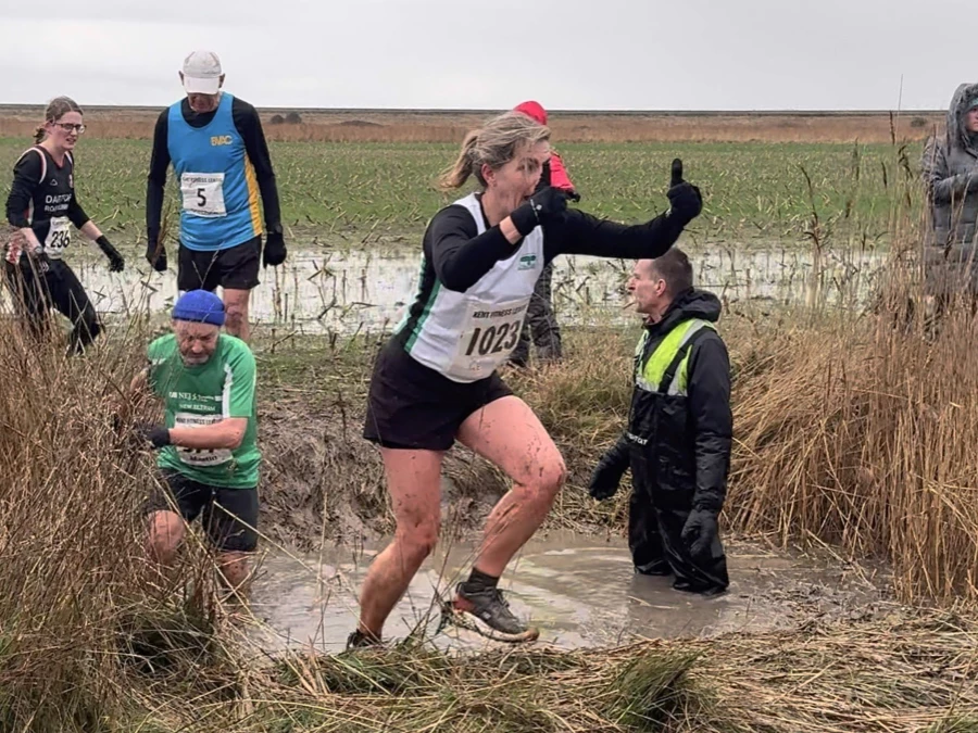 KFL Minnis Bay 2024 - Kent Fitness League runners in action crossing a muddy ditch. Maidstone Harriers