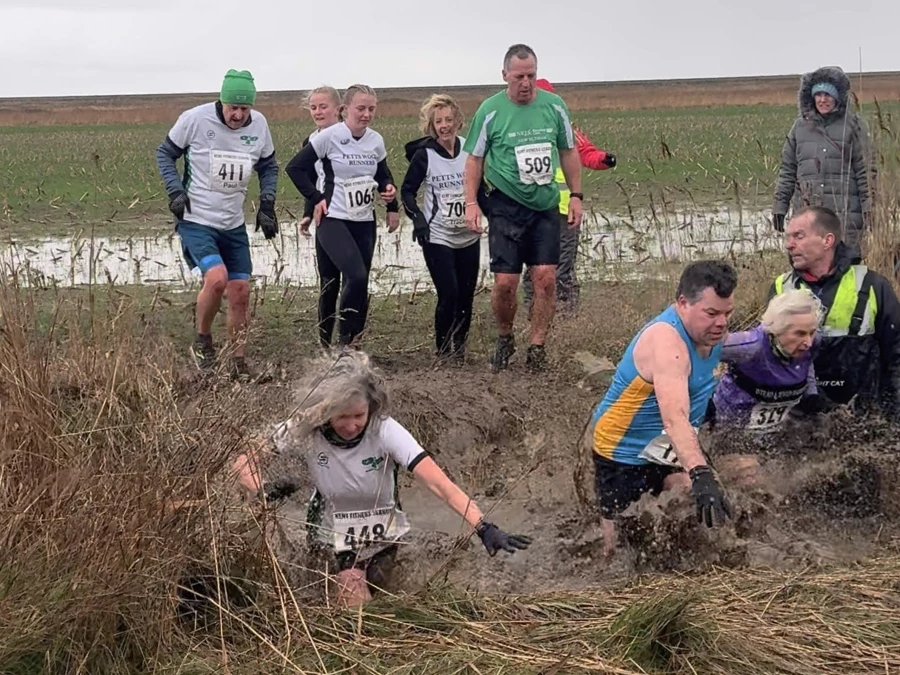 KFL Minnis Bay 2024 - Kent Fitness League runners in action crossing a muddy dyke. Maidstone Harriers