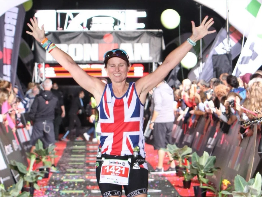 Maidstone Harriers' Sally Howson crosses the line at Ironman Copenhagen 2018 with arms raised, race clock showing 13:36:10.