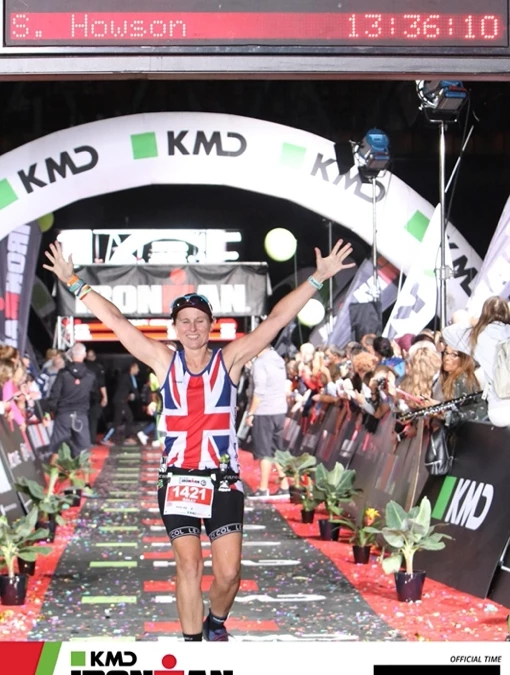 Maidstone Harriers' Sally Howson crosses the line at Ironman Copenhagen 2018 with arms raised, race clock showing 13:36:10.