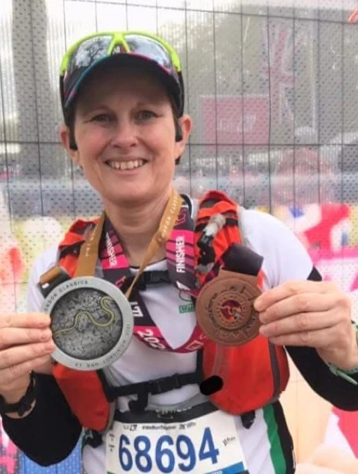 Maidstone Harriers' Sally Howson holding her London Marathon 2024 finisher medal and the London Classics medal, smiling at the event village.