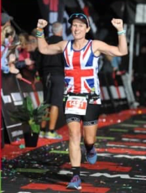 Maidstone Harriers' Sally Howson running down a finish chute with arms raised, wearing a Union Jack vest