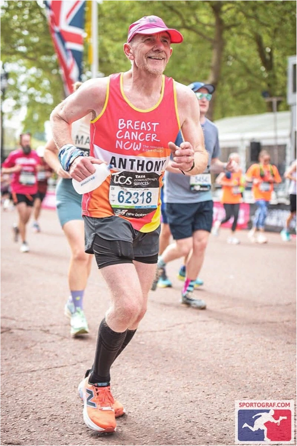 Anthony Bishop running the TCS London Marathon in a Breast Cancer Now vest, smiling near the finish