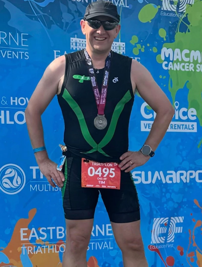 Tim Hilder of Maidstone Harriers smiling with his finisher's medal in front of the Eastbourne Triathlon photowall