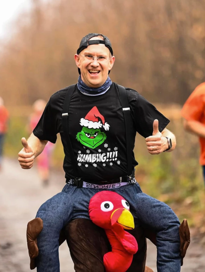 Tim Hilder giving a double thumbs up in a turkey costume and Grinch t-shirt at the Maidstone Harriers Turkey Run
