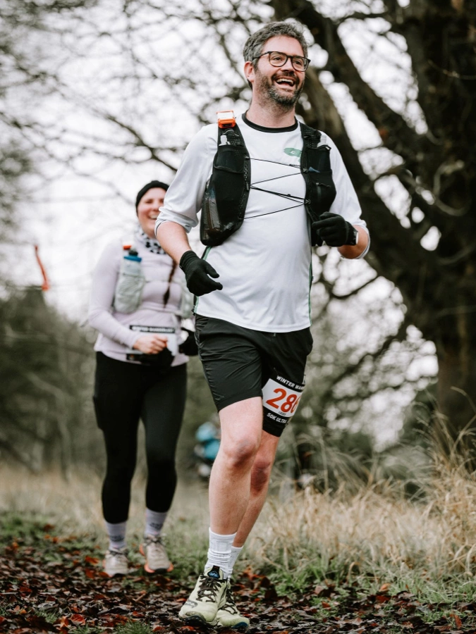 Oscar Phillips-Barrett running a mountain trail in heavy rain, wearing waterproofs, Maidstone Harriers white shirt, and a hydration vest at a Trail Events Co race.