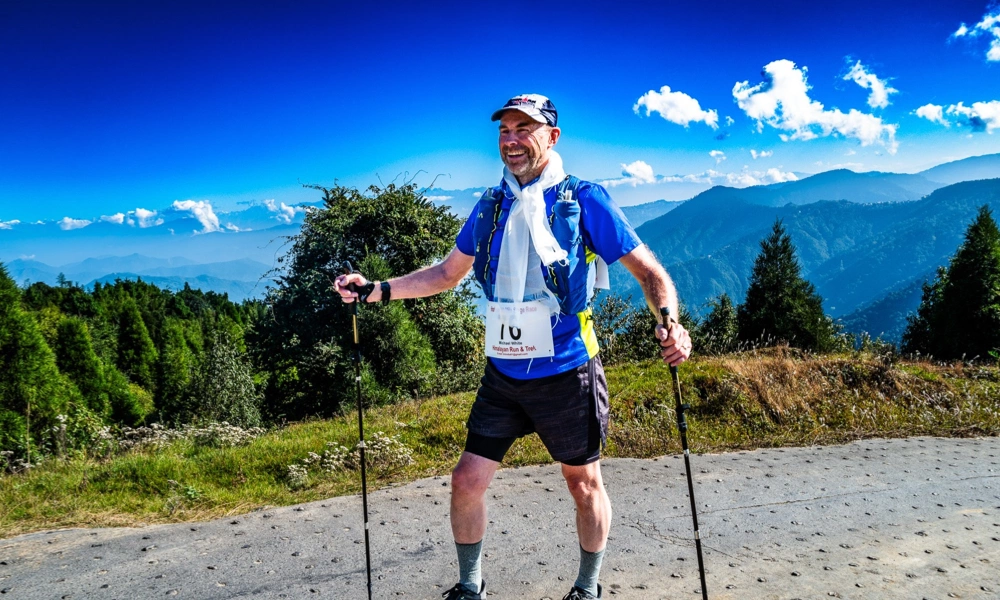 Michael White on a mountain section of the Himalayan 100 Mile Stage Race with trekking poles and mountain views behind him