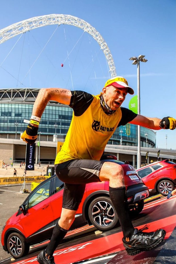 Michael White running up an inclined obstacle in front of cars parked on the steep incline, with Wembley Stadium in the background