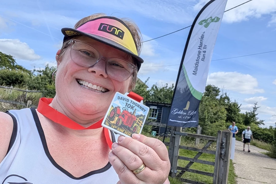 Catey Bowles smiling with her David Thornby 10K 2026 medal by the Maidstone Harriers flag