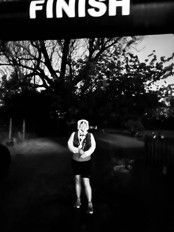 Maidstone Harriers runner Jo Smit standing under a finish arch at dusk after completing an ultramarathon